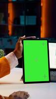 Vertical Video African american girl holding tablet with greenscreen layout, conducting data analysis for financial or economics courses. Student uses isolated mockup display on device, work from home. Camera B.