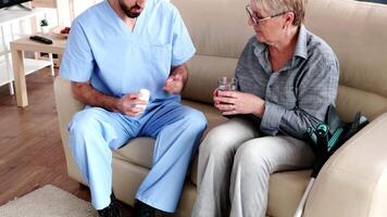 Male nurse on couch with elderly retired woman giving her medical treatment in retirement home. video