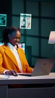 Vertical Video African american student working on her bachelor paper essay at home, writing ideas from online research. Girl exploring digital libraries and academic databases for additional resources. Camera B.