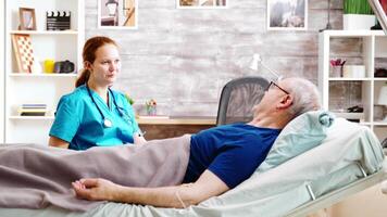 Sick elderly man having a conversation with a caucasian nurse while lying in a hospital bed in a nursing home video