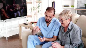 Male nurse in retirement home helping elderly woman to use her phone. video