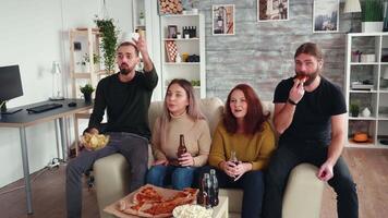 caucasico amici godendo loro tempo insieme mentre applauso per loro calcio squadra. amici mangiare patatine fritte e potabile birra. video