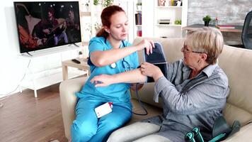 Female nurse measuring blood pressure of elderly woman in retirement home sitting on sofa video