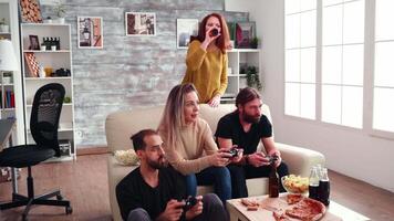 Happy group of cheerful male and female friends playing online video games using wireless controller.