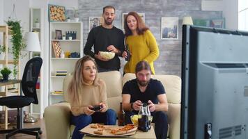 joven Pareja comiendo palomitas de maiz mientras su amigos son jugando vídeo juegos en televisión utilizando inalámbrico controladores video