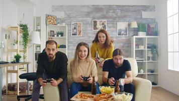 Group of friends relaxing together in living room playing video games using wireless controllers.