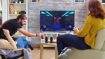 Back view of young woman playing video games on tv with her friends in living room using wireless controller. Happy friendship.