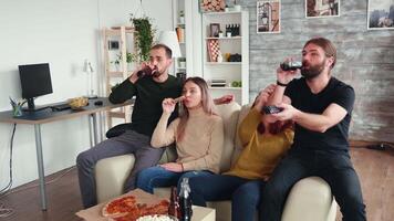 grupo de cerca amigos disfrutando su cerveza y Pizza mientras acecho un película en televisión sentado en sofá. video