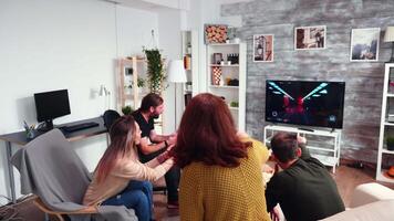 Blonde woman sitting on a chair playing video games using wireless controller and having fun with her friends.