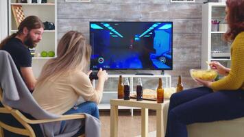 Back view of blonde woman playing shooter games while her friends are eating pizza. Playing games with wireless controller. video