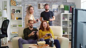 Two girl laughing while playing video games with their friend on tv using wireless controllers.