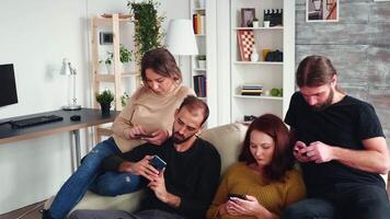 gebaard Mens zittend Aan de bankstel in leven kamer browsen Aan zijn telefoon samen met zijn saai vrienden. video