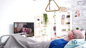 Retired old man lying in bed in a nursing home watching tv. video