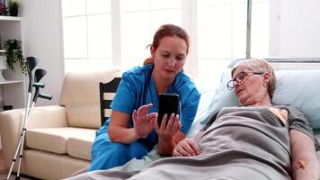 hembra enfermero Ayudar antiguo mujer a utilizar teléfono inteligente en enfermería hogar. video