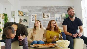 Group of friends laughing hard while a sitcom on tv in living room. Pizza and popcorn on table. video