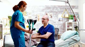 Nurse helping a disabled retired old man to stand up from his hospital bed in a bright and cozy nursing retirement home video