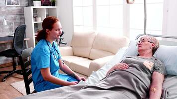 im Ruhestand alt Frau Lügen auf Bett im Pflege- Zuhause reden mit weiblich Krankenschwester. video
