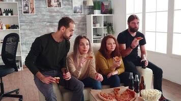 grupp av vänner Sammanträde på soffa äter pizza, dricka öl och ser koncentrerad på en film på tv. video