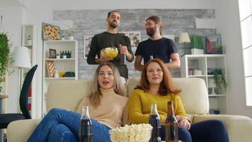 jong Dames zittend Aan bankstel glimlachen terwijl aan het kijken TV terwijl de jongens aan het eten chips en hebben een mooi zo tijd. video