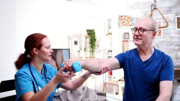 Female nurse in retirement home helping an old man to recover from an accident with dumbells video