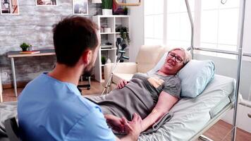 Retired old woman lying in hospital ned in a retirement home talking with caucasian male nurse video