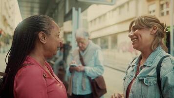 two women talking and smiling in front of a bus video