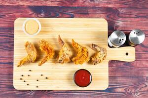 Crispy chicken wings with tomato sauce and mayo dip isolated on cutting board side view of fastfood photo