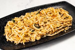 Spicy vegetable chow mein in a black tray isolated on marble background top view of chinese food photo