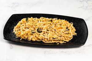 Spicy vegetable chow mein in a black tray isolated on marble background top view of chinese food photo