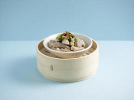 steamed spare ribs with black bean sauce and minced garlic served in a wooden bowl with chopsticks isolated on mat side view on grey marble background photo