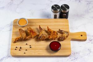 Crispy chicken wings with tomato sauce and mayo dip isolated on cutting board side view of fastfood photo