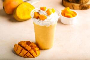Mango milkshake with cream and raw fruit slice served in glass isolated on table top view healthy morning drink photo