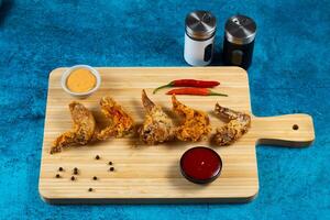 Crispy chicken wings with tomato sauce and mayo dip isolated on cutting board side view of fastfood photo