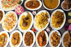 Mutton Bhuna, Jali Kabab, khichuri, Shrimp Biryani, Duck Bhuna Khichuri, hisla Pulao, mutton biriyani, chicken korma, Loitta Fry, Chingri Bhuna, Salad, Fruits Custard top view of bangladesh food photo