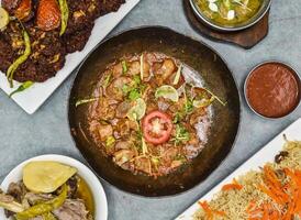 Assorted pakistani food lambr or dumb karahi, chapli kabab, roash, dum pukht, kabuli pulao, chilli sauce and butter chicken makhni served in dish isolated on background top view photo