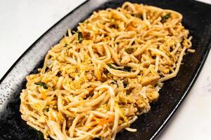 Spicy vegetable chow mein in a black tray isolated on marble background top view of chinese food photo