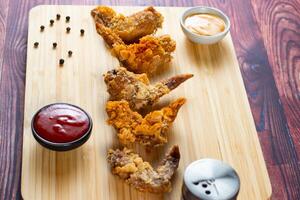 Crispy chicken wings with tomato sauce and mayo dip isolated on cutting board side view of fastfood photo