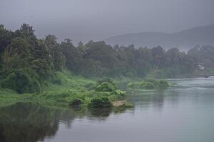 A landscape view of a calm river with green trees and mountain in India photo
