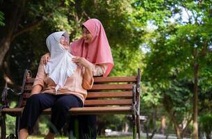 musulmán Cuidado cuidador o enfermero tomando cuidado de el paciente en el hospital parque. contento musulmán madre en hijab abrazando hija. concepto de ahorros y mayor salud seguro, un contento familia foto