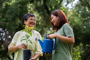 Portrait, Asian family mom and daughter plant sapling tree outdoors in nature park, Concept of happy retirement With care from a caregiver and Savings and senior health insurance, Happy family photo