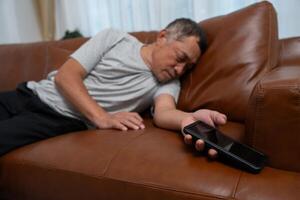 Senior male asian presses hand to his chest has a heart attack suffers from unbearable pain in the living room, lonely men try using the smartphone to call for Emergency help. photo