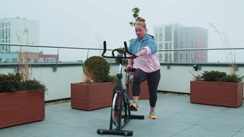 Athletic woman riding on spinning stationary bike training routine on house rooftop, weight loss video