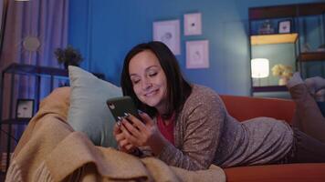 Woman lying on sofa at home using mobile phone communicating in social network or online shopping video