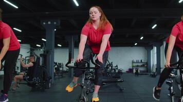 grupo do meninas executa aeróbico Treinamento exercite-se cardio rotina em bicicleta simuladores, ciclo Treinamento video