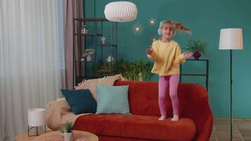 Happy child girl kid in headphones dancing and jumping while listening to the music at home alone video