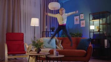 Active funny girl kid jumping, dancing, fooling on soft cozy sofa at home spend free time alone video