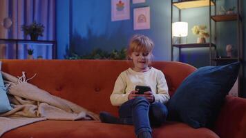 Child toddler hold smartphone watching funny cartoons, chatting with friends on couch alone at home video