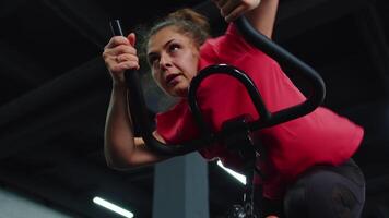 portret Kaukasisch vrouw oefenen training Aan stationair wielersport machine fiets in Sportschool, langzaam beweging video