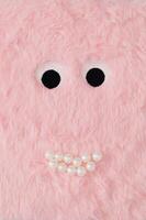 Cute fluffy monster made with pastel pink faux fur and white pearls. Minimal concept. Creative funny face composition. An original cute fluffy monster background image idea. Flat lay, top of view. photo