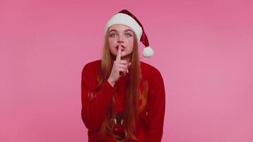 Woman wears red Christmas sweater presses index finger to lips makes silence gesture sign, secret video